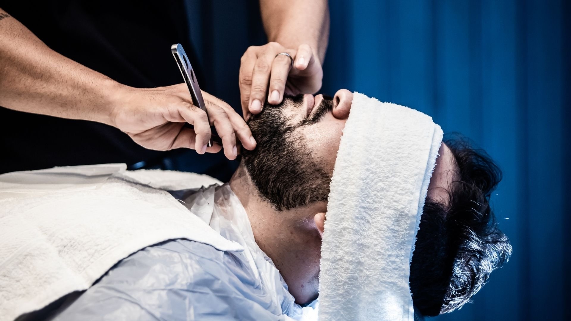 Barber trimming beard of client with clippers and towel