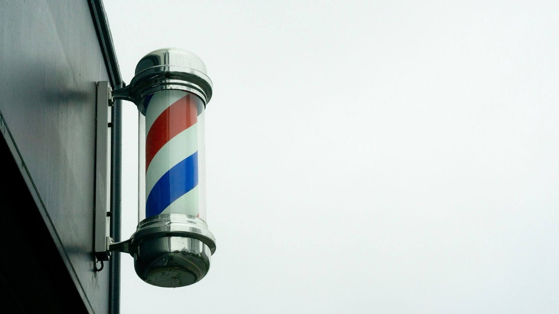Classic barbershop pole with red, white, and blue spiral stripes mounted on wall
