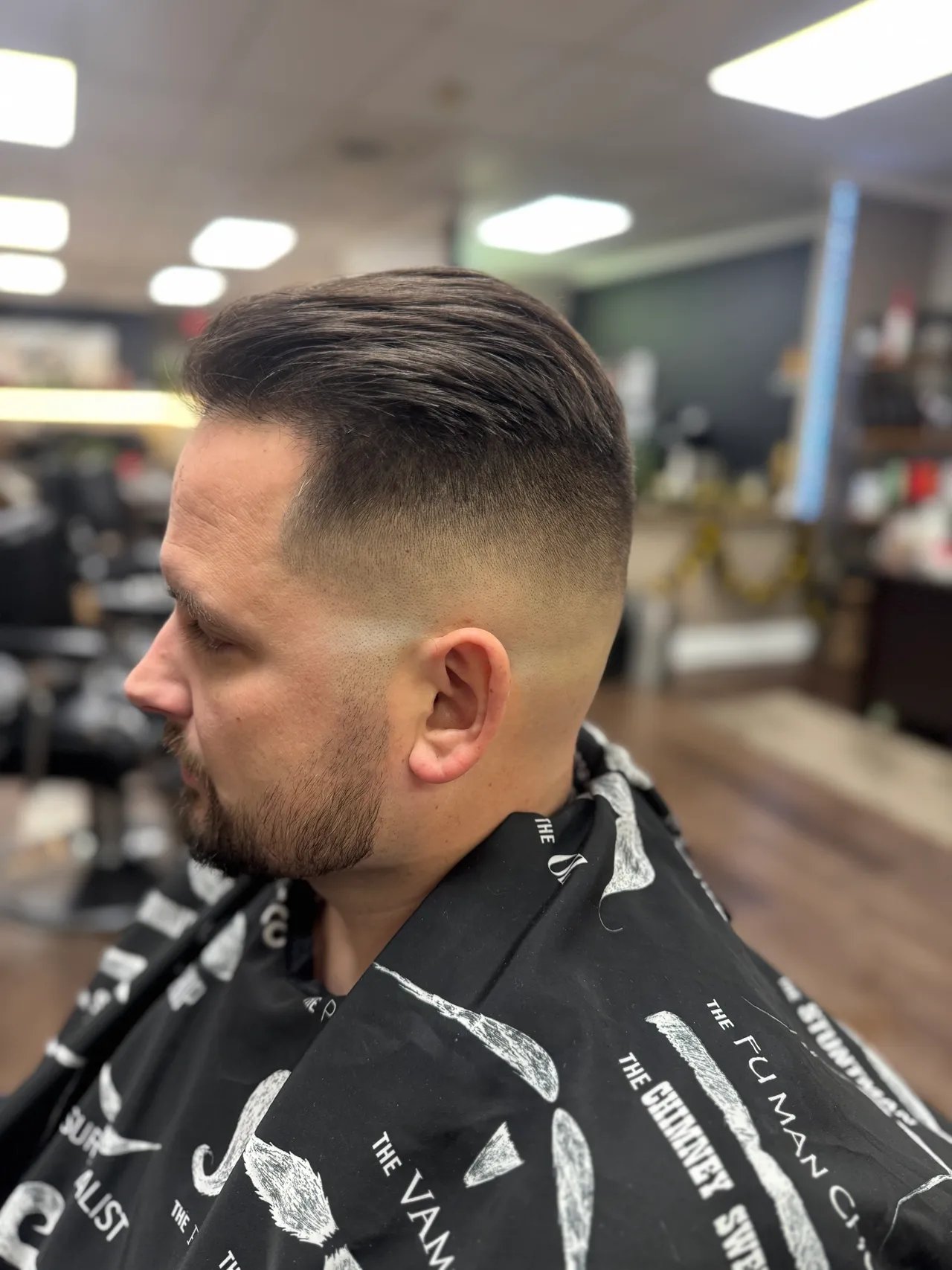 Man with fade haircut and beard in barbershop wearing patterned black cape