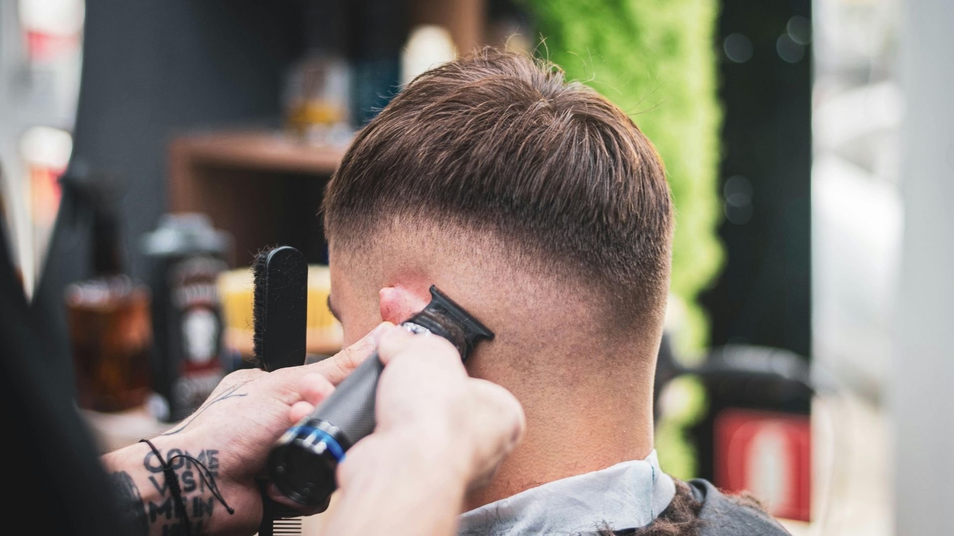 Barber using electric trimmer to cut client's short brown hair on sides