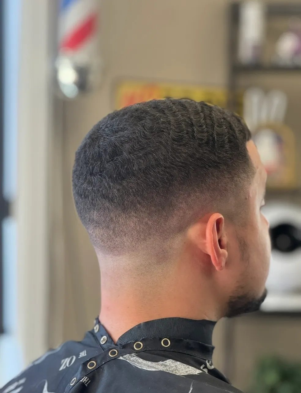 Man with short, textured haircut in barbershop, rear view of neat fade hairstyle