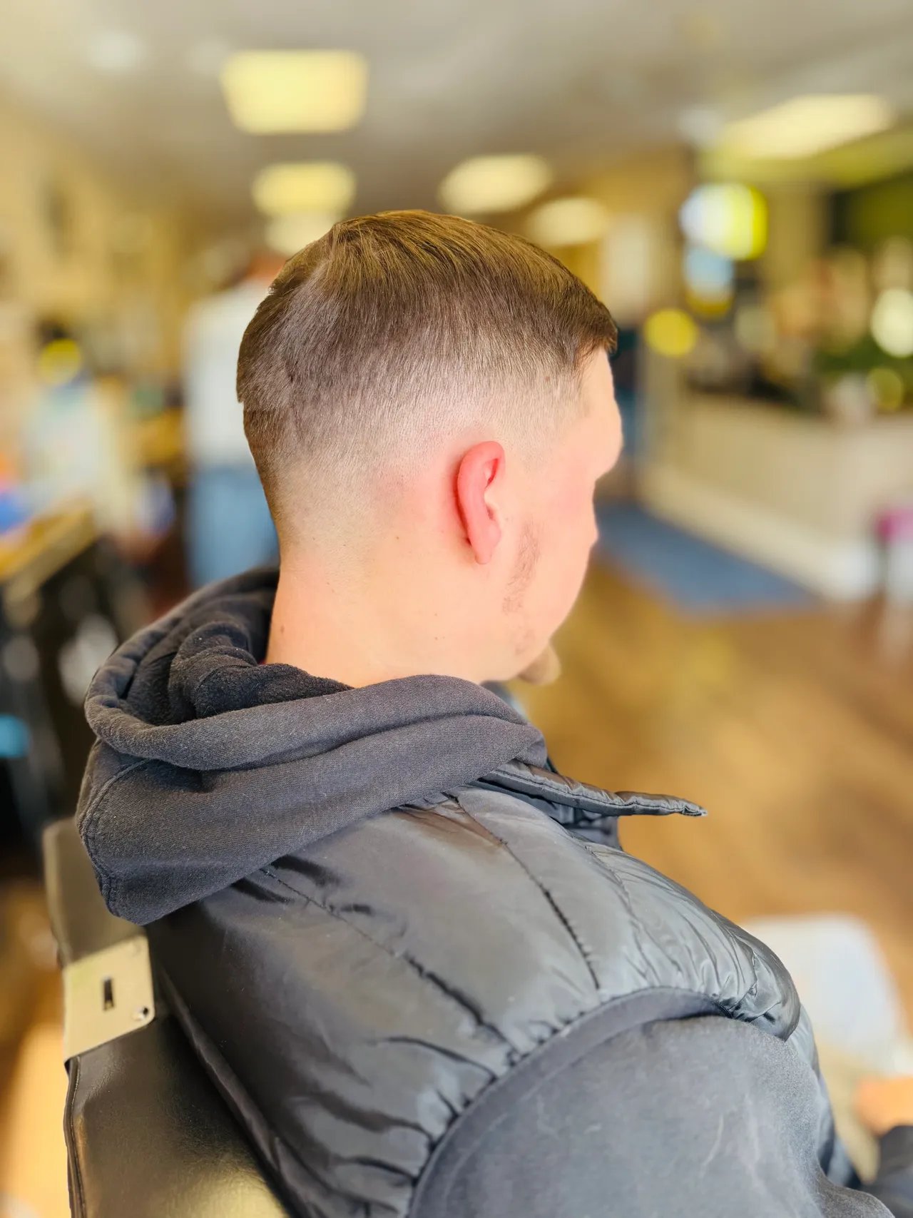 Back view of young boy with short haircut wearing dark jacket indoors