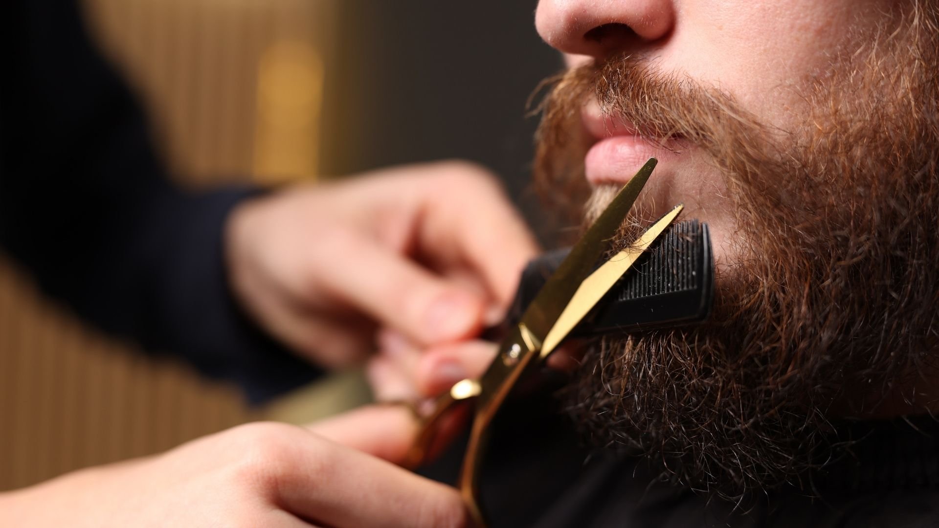 Barber trimming man's full beard with electric clippers during haircut